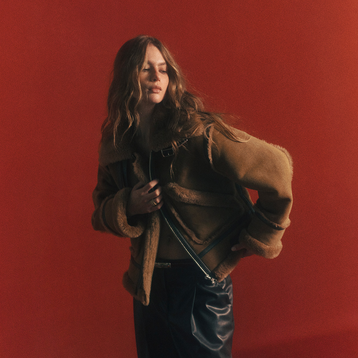 a brown-haired model wearing black faux leather pants and a brown coat